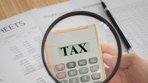 an image showing a magnifying glass zooming in on some tax papers and the word tax written in large font