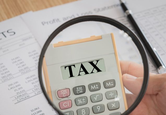 an image showing a magnifying glass zooming in on some tax papers and the word tax written in large font